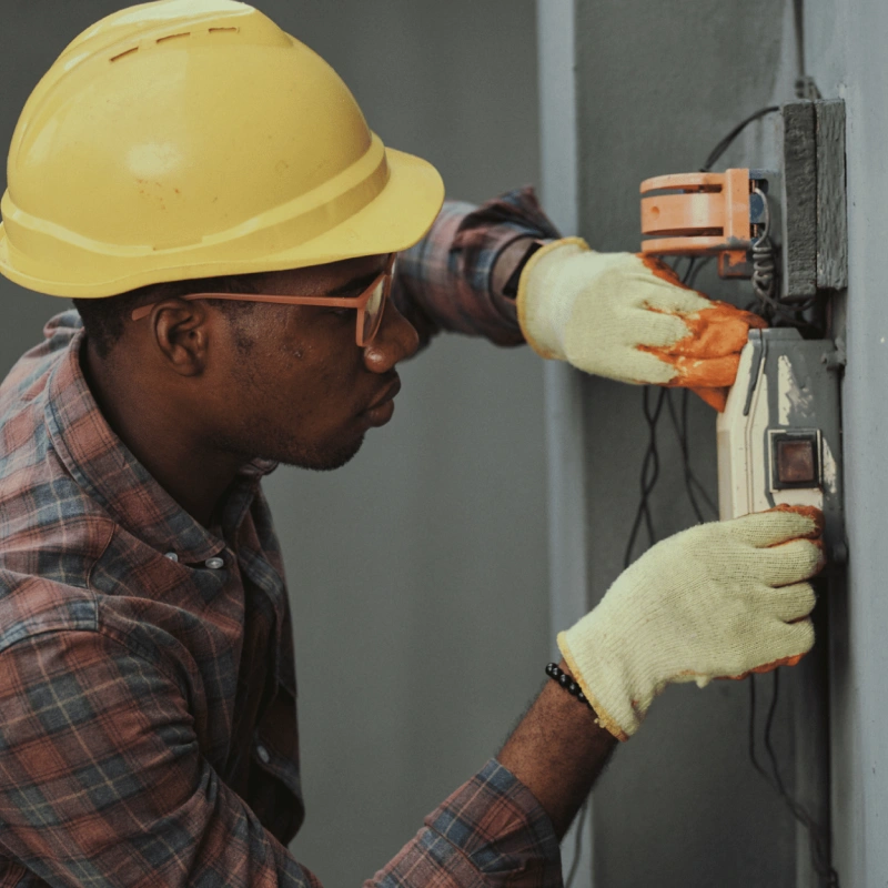 person fixing eletrical panel in yellow hard hat